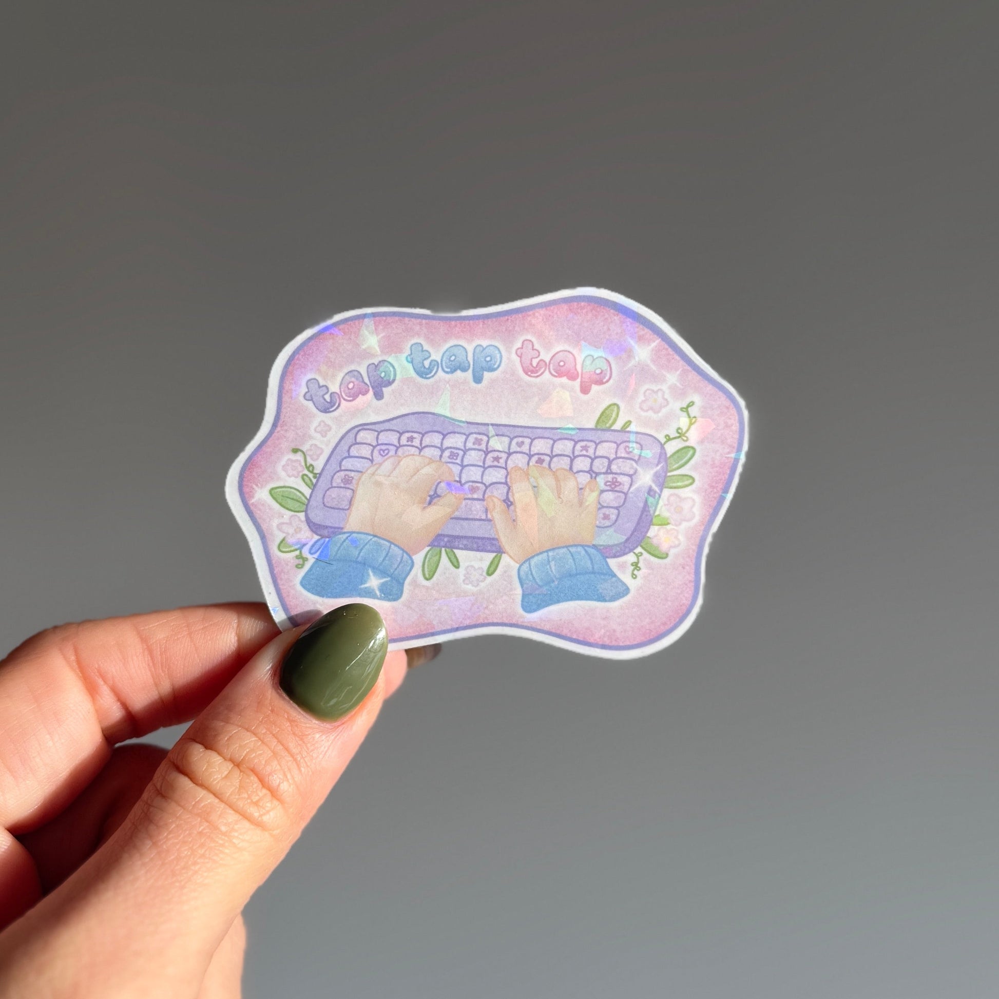 Holographic sticker showing hands typing on a keyboard with the text 'tap tap tap'. For the focused, cozy worker in flow state. Waterproof die-cut sticker from Klari Store.